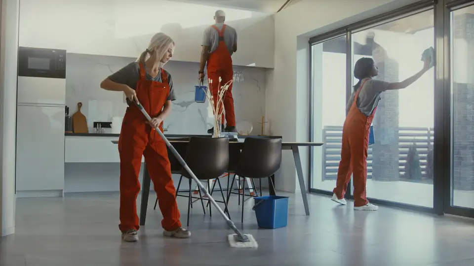 Cleaners in red overalls mopping the floor and wiping the windows of an office kitchen