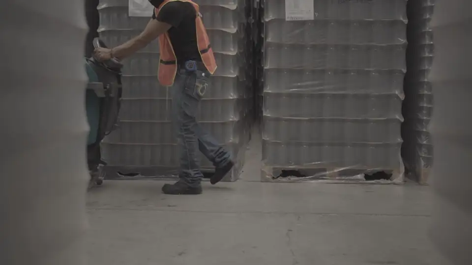 A worker guiding a walk-behind floor scrubber across a warehouse floor