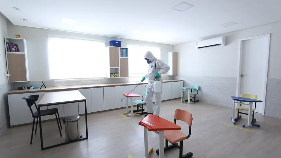 A cleaner in protective gear disinfecting an empty classroom
